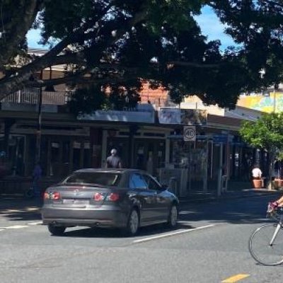 A cyclist rides across a busy road in the Brisbane suburb of West End, with a car passing in the other lane.